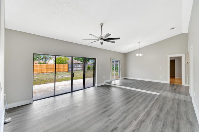 empty room featuring ceiling fan with notable chandelier, high vaulted ceiling, wood finished floors, and baseboards