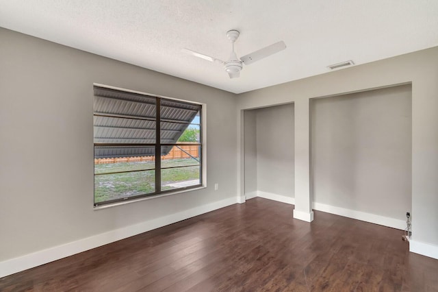 unfurnished bedroom featuring baseboards, visible vents, ceiling fan, wood finished floors, and multiple closets