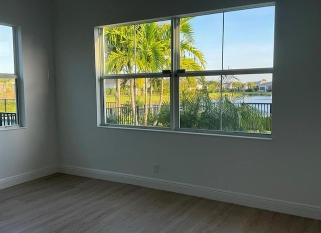 spare room with plenty of natural light, a water view, wood finished floors, and baseboards