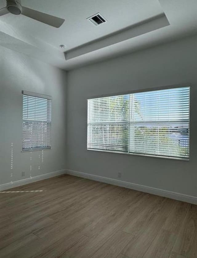 empty room featuring a tray ceiling, a healthy amount of sunlight, visible vents, and wood finished floors