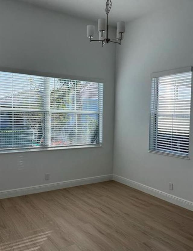 spare room featuring plenty of natural light, wood finished floors, an inviting chandelier, and baseboards