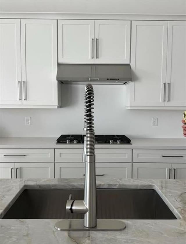 kitchen with black gas cooktop, range hood, light stone counters, and white cabinets