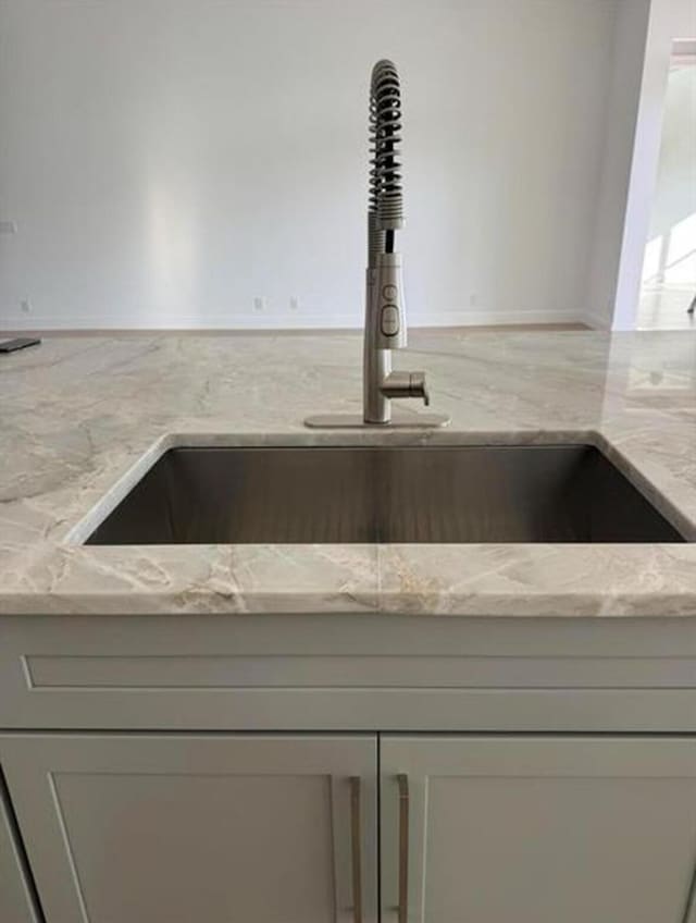 interior details with gray cabinets, a sink, and light stone countertops