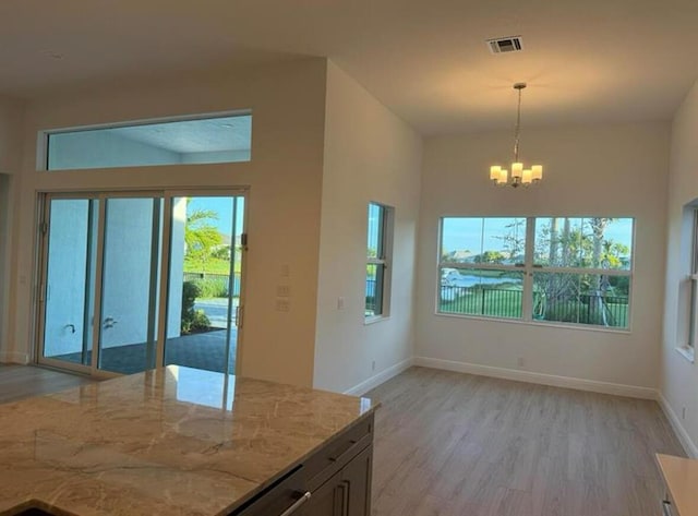 kitchen with light stone counters, visible vents, baseboards, light wood-style floors, and hanging light fixtures