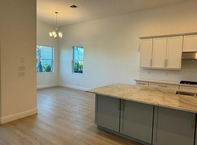 kitchen with under cabinet range hood, visible vents, white cabinets, light stone countertops, and decorative light fixtures