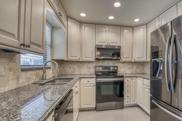 kitchen featuring stainless steel appliances, backsplash, light tile patterned flooring, a sink, and dark stone countertops