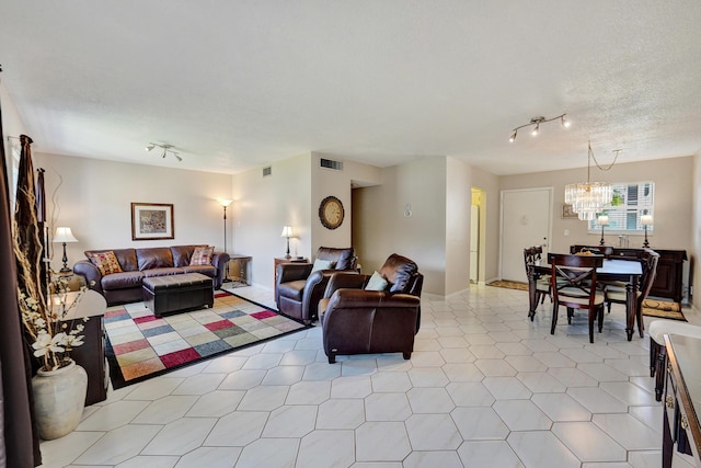 living area featuring rail lighting, visible vents, a textured ceiling, and an inviting chandelier