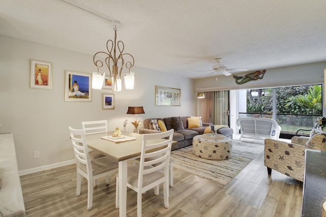 dining room featuring ceiling fan with notable chandelier, baseboards, and wood finished floors