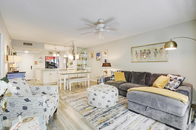 living area featuring light wood-style floors, visible vents, baseboards, and ceiling fan with notable chandelier