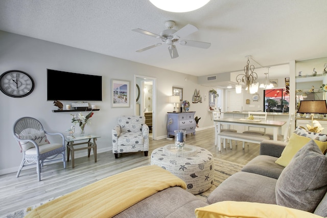 living room with a textured ceiling, light wood-style flooring, ceiling fan with notable chandelier, visible vents, and baseboards