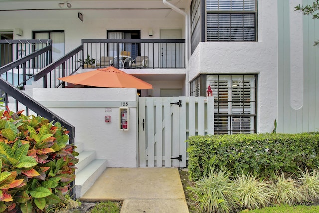 entrance to property with a balcony, fence, a gate, and stucco siding