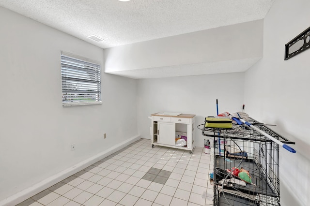 interior space with a textured ceiling, light tile patterned flooring, visible vents, and baseboards