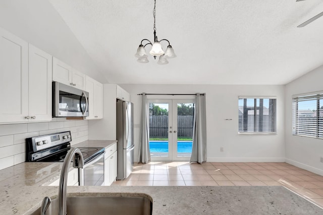 5598 Pebble Brook Ln, Boynton Beach, FL 33472 - kitchen with light tile patterned floors, stainless steel appliances, white cabinetry, vaulted ceiling, and light stone countertops