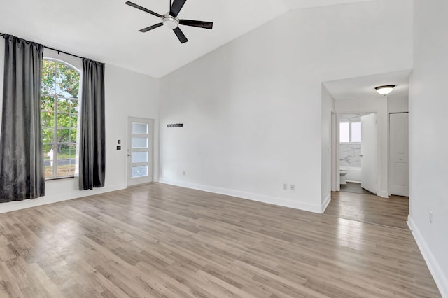 empty room with high vaulted ceiling, light wood-type flooring, ceiling fan, and baseboards