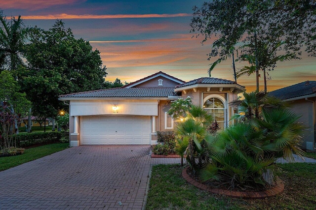 view of front of home with an attached garage, a tiled roof, decorative driveway, and stucco siding