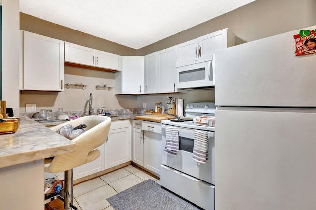 kitchen featuring white appliances, white cabinetry, a sink, and light tile patterned flooring