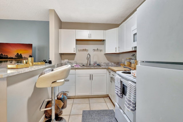 kitchen featuring white appliances, white cabinets, a sink, and light tile patterned floors