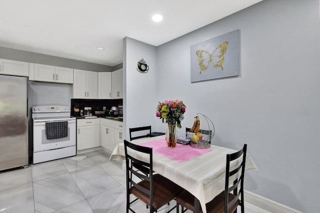 kitchen featuring white electric stove, dark countertops, stainless steel refrigerator, and white cabinetry