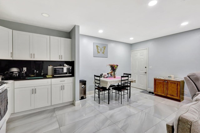 kitchen with tasteful backsplash, dark countertops, stainless steel microwave, white cabinetry, and a sink