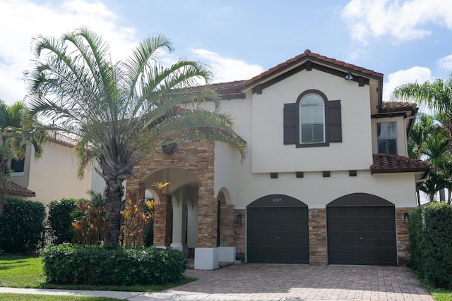 mediterranean / spanish home featuring stone siding, a tile roof, and stucco siding