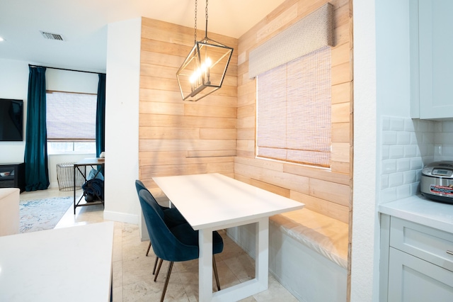 dining space featuring light tile patterned floors, wooden walls, visible vents, and a notable chandelier