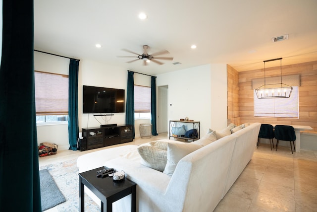 living room featuring ceiling fan with notable chandelier, wooden walls, visible vents, and recessed lighting