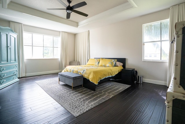 bedroom with dark wood-style floors, a tray ceiling, crown molding, ceiling fan, and baseboards