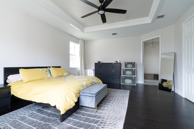 bedroom with a tray ceiling, dark wood finished floors, visible vents, ornamental molding, and baseboards