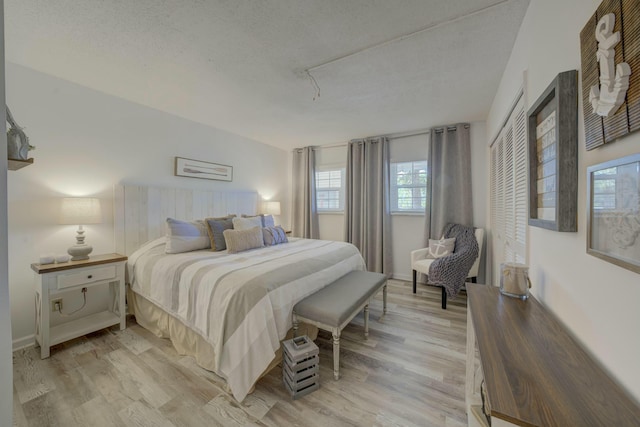 bedroom with a textured ceiling, light wood-style flooring, and baseboards