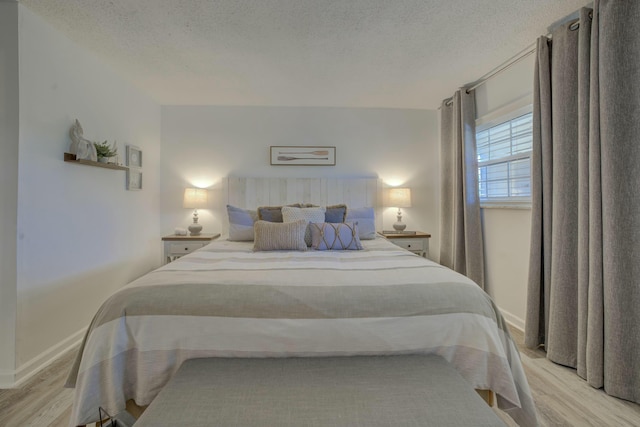 bedroom with light wood-style flooring, baseboards, and a textured ceiling