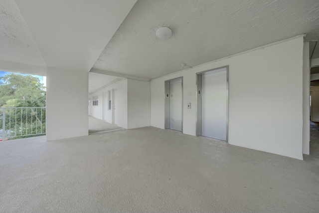 interior space with a textured ceiling, speckled floor, and elevator