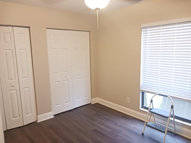 unfurnished bedroom featuring multiple closets, dark wood finished floors, and baseboards