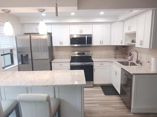 kitchen featuring light stone counters, stainless steel appliances, a sink, white cabinets, and hanging light fixtures