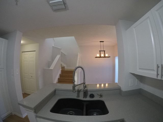 kitchen featuring pendant lighting, visible vents, an inviting chandelier, white cabinets, and a sink