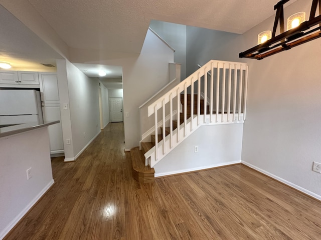 stairs with a textured ceiling, baseboards, and wood finished floors