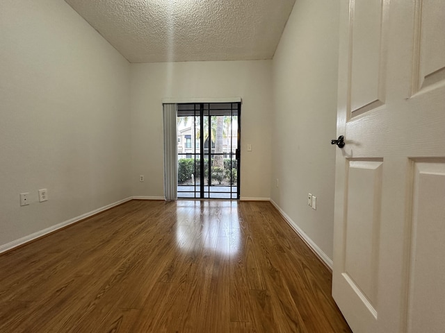 empty room featuring a textured ceiling, wood finished floors, and baseboards