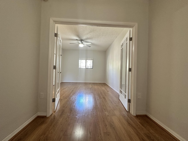 empty room with a ceiling fan, a textured ceiling, baseboards, and wood finished floors