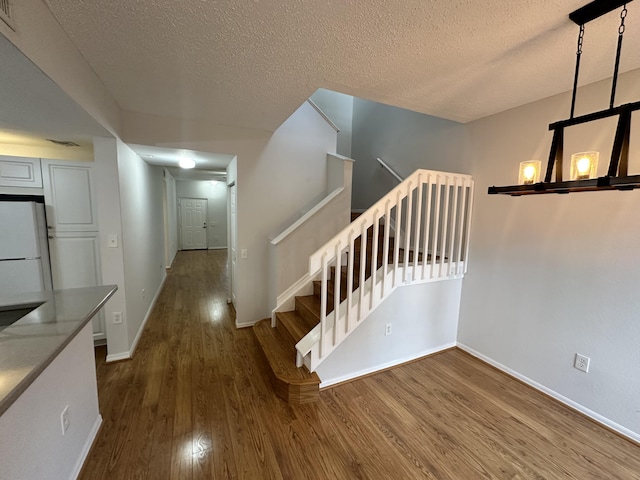 staircase with visible vents, a textured ceiling, baseboards, and wood finished floors