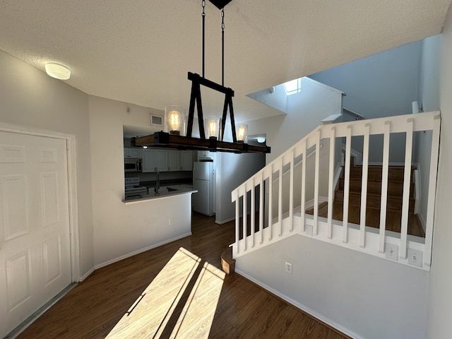 stairway with visible vents, a textured ceiling, an inviting chandelier, and wood finished floors