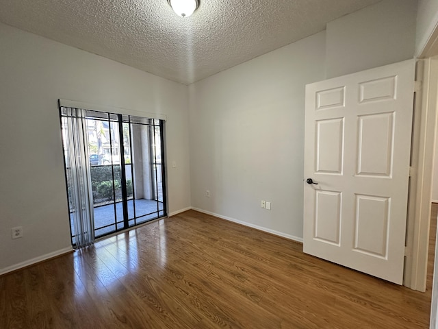 empty room featuring a textured ceiling, wood finished floors, and baseboards