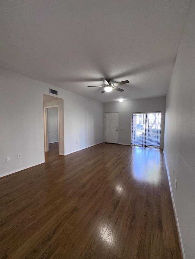 unfurnished living room with baseboards, visible vents, ceiling fan, dark wood-type flooring, and a textured ceiling