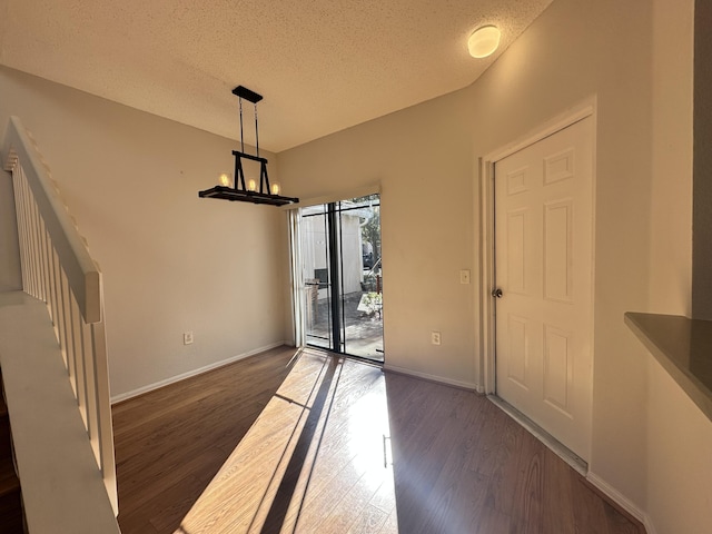 unfurnished dining area featuring dark wood-style floors, a textured ceiling, an inviting chandelier, and baseboards