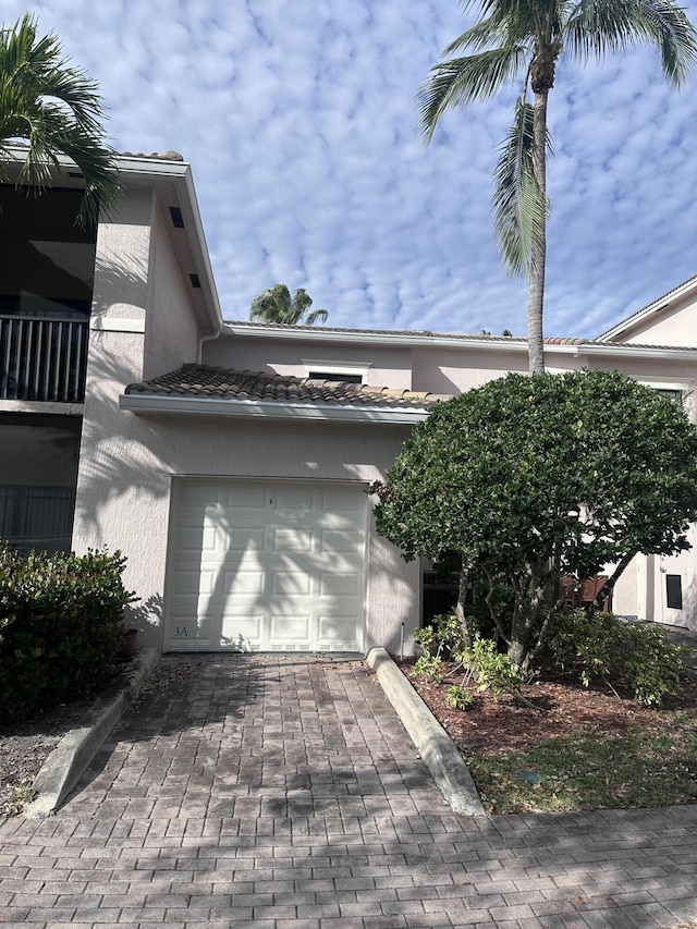 view of side of home with decorative driveway, a tile roof, an attached garage, and stucco siding