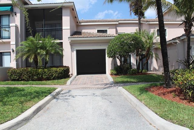 view of front of house featuring a garage, a tile roof, decorative driveway, stucco siding, and a front yard