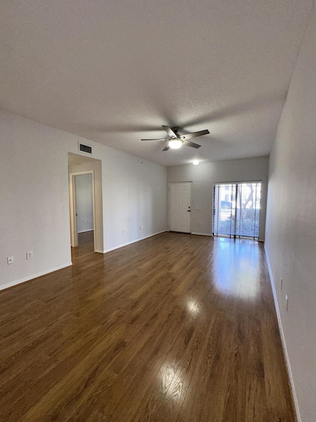 unfurnished living room with baseboards, visible vents, a ceiling fan, dark wood-style flooring, and a textured ceiling