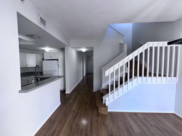 stairs with a textured ceiling, wood finished floors, visible vents, and baseboards