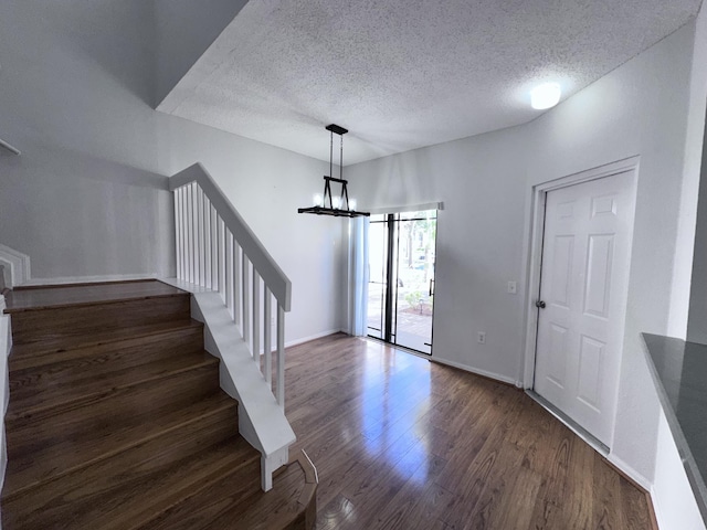 entrance foyer featuring dark wood finished floors, a notable chandelier, stairway, a textured ceiling, and baseboards