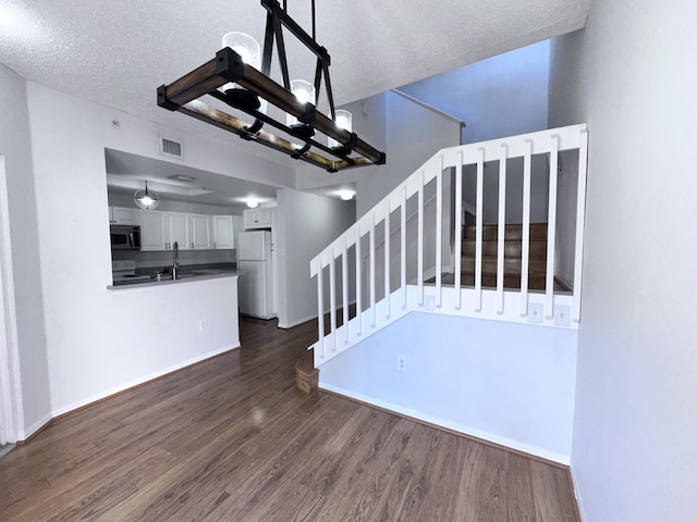 staircase featuring a textured ceiling, wood finished floors, visible vents, and an inviting chandelier