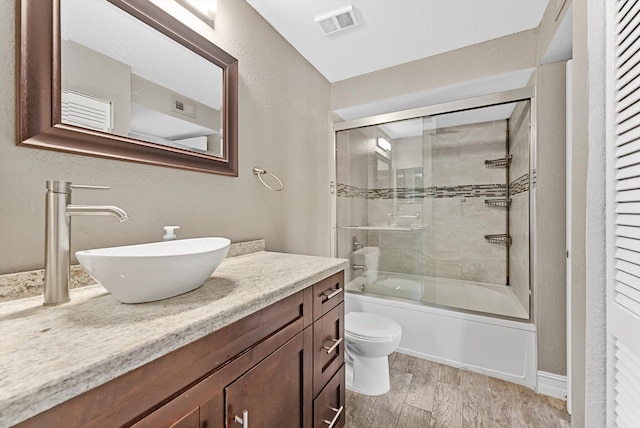 full bathroom featuring visible vents, toilet, wood finished floors, combined bath / shower with glass door, and vanity