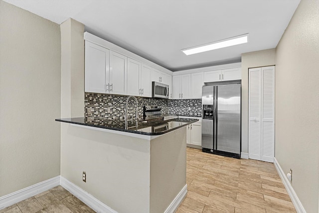 kitchen with a peninsula, appliances with stainless steel finishes, white cabinetry, and decorative backsplash